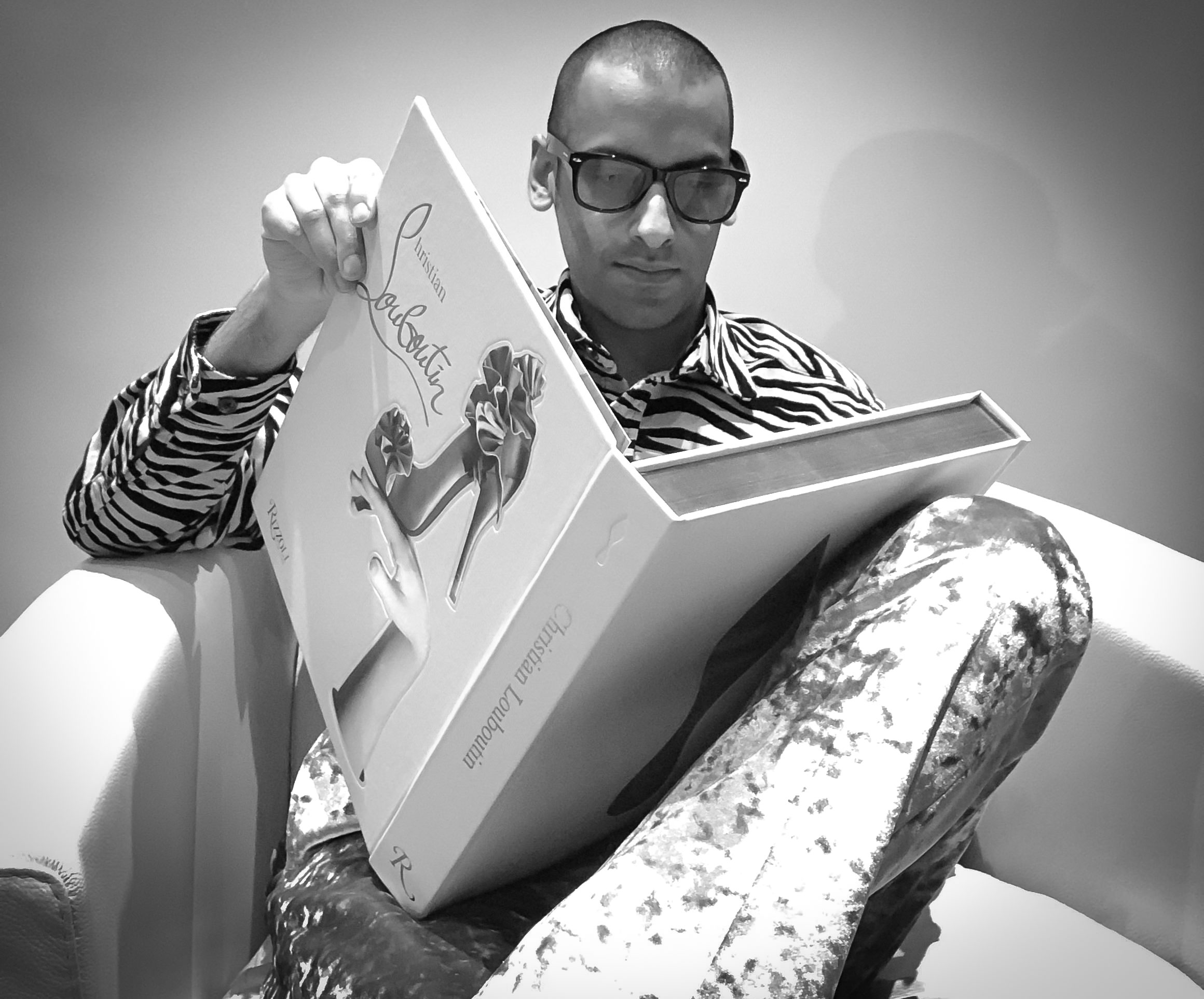 Stylish man reading a Christian Louboutin fashion book in an armchair