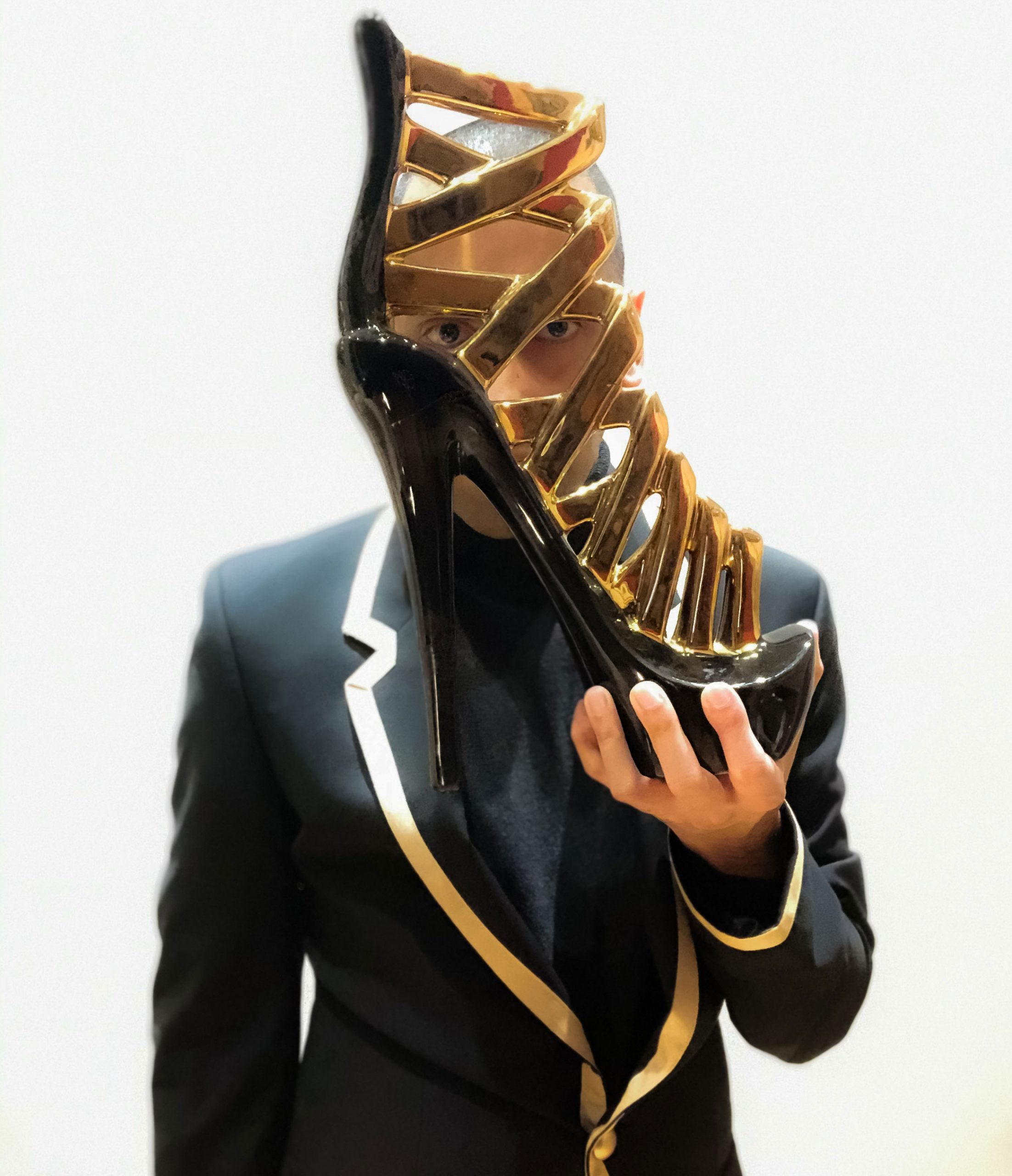 Holding a stiletto high heel shoe home decor ornament whilst eye gazing and dressed in an elegant black and gold blazer